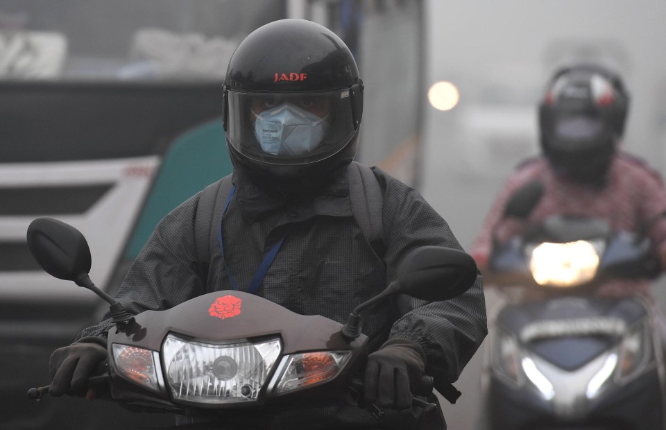 A moped driver makes his way through the city while wearing a breathing mask