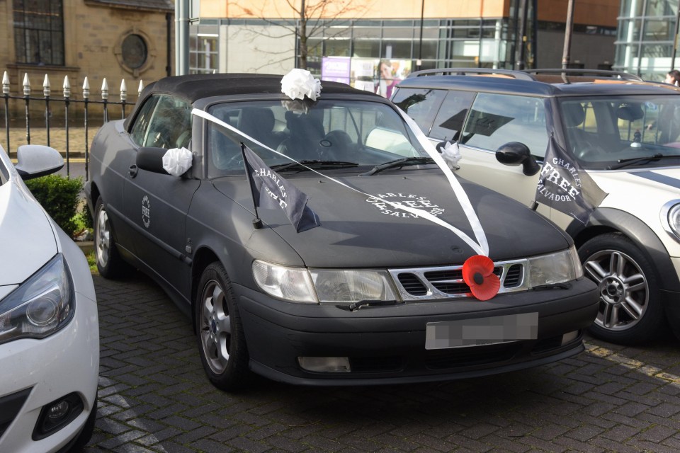 A black Saab convertible parked outside has ‘Free Charles Salvador’ emblazoned on the bonnet and side