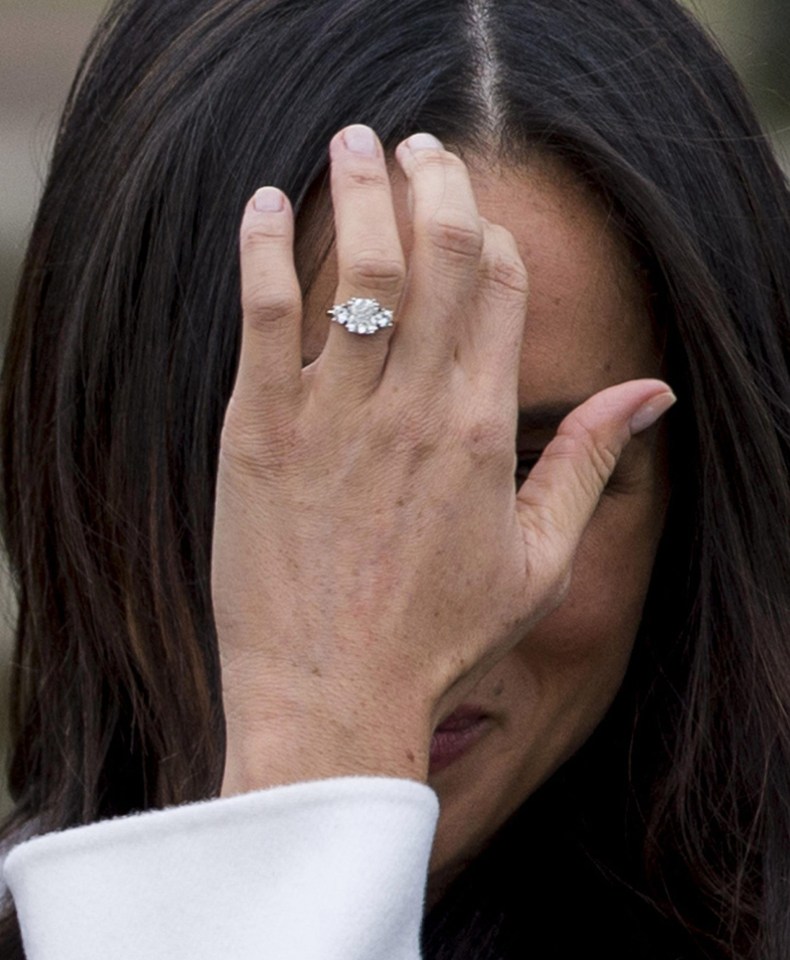 Meghan shows off her diamond ring, designed by Prince Harry, as she pushes her hair back during photocall at Kensington Palace