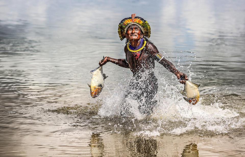  A proud Bejà Kayapó man makes his way through the Xingu River with a fish in each hand after a successful expedition