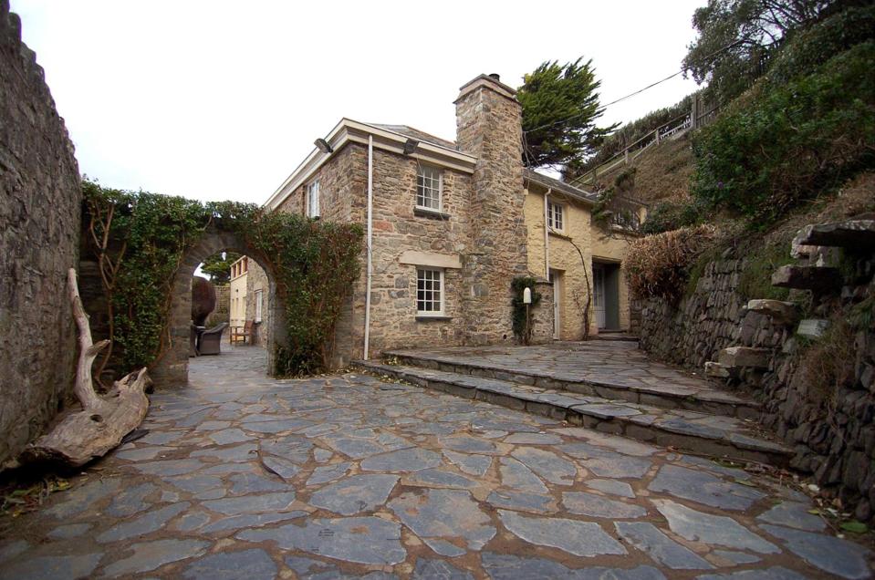  An arched door in a stone wall with paved pathways leads the way to the front door