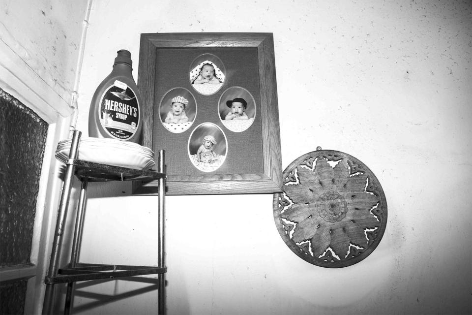  A bottle of syrup stands next to a collection of baby photos on a grimy wall