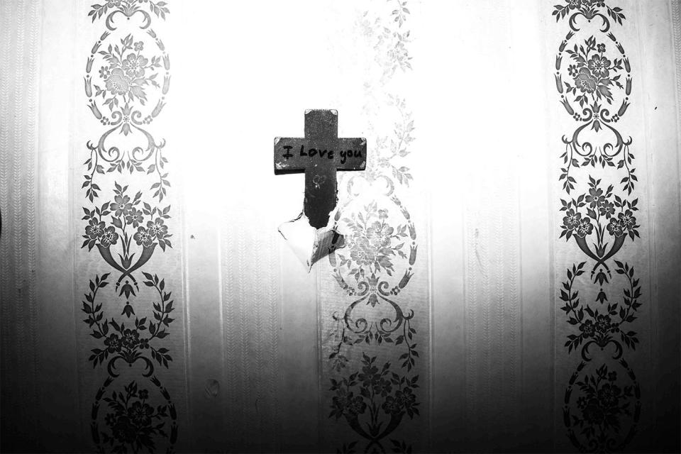  A crucifix with the words I Love you is attached to a wall which has wallpaper peeling from it