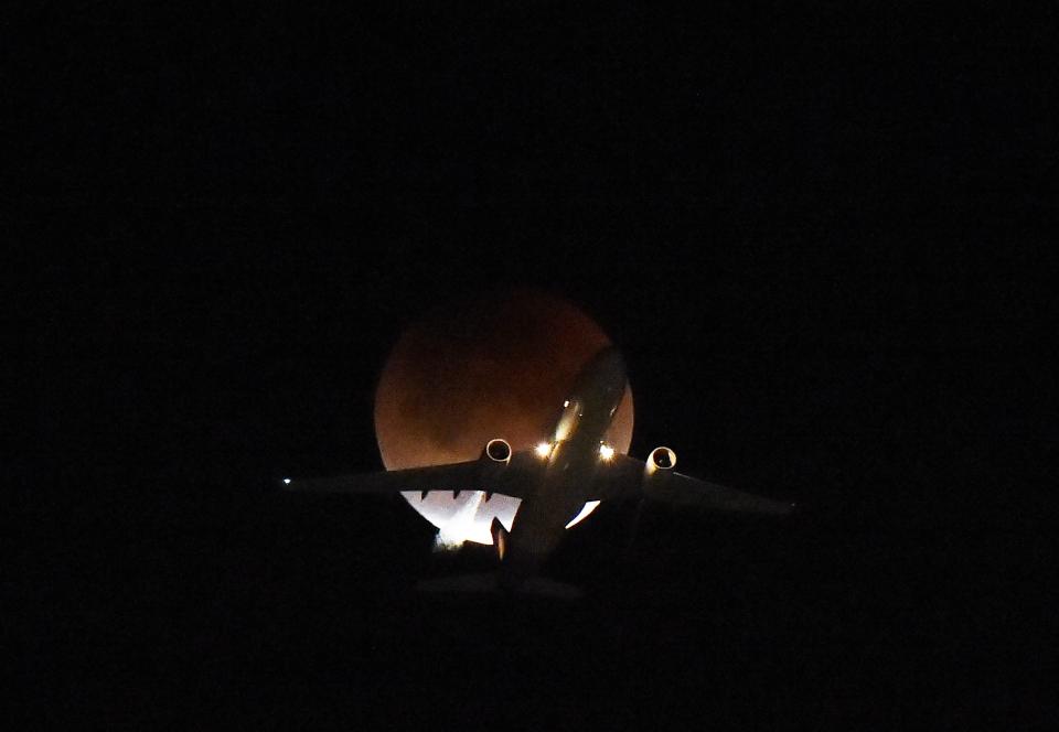  A plane flies passing the creepy looking moon over LA