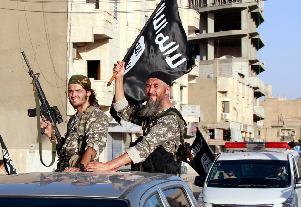 Militant ISIS fighters wave flags as they take part in a military parade along the streets of Syria’s northern Raqqa province