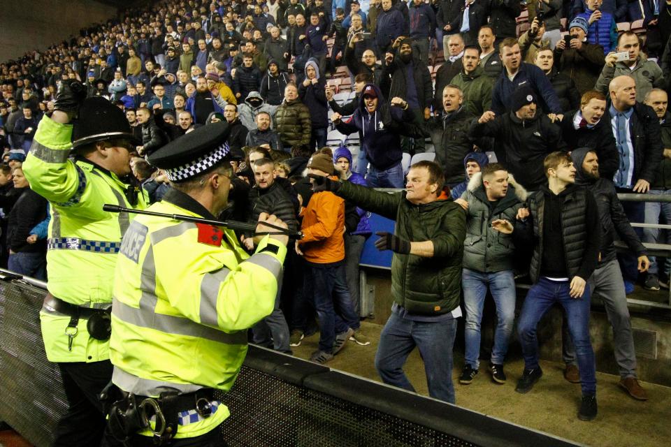  A police officer has to withdraw a baton as they are confronted by an angry fan at the DW Stadium