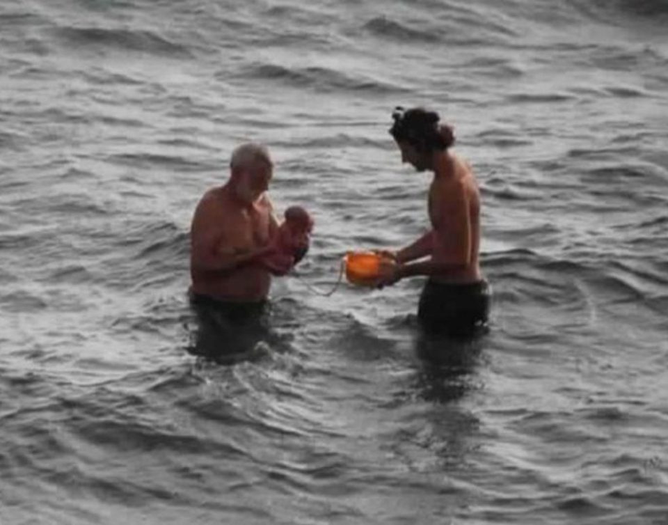 A husband and doctor hold a baby after it was delivered in the sea