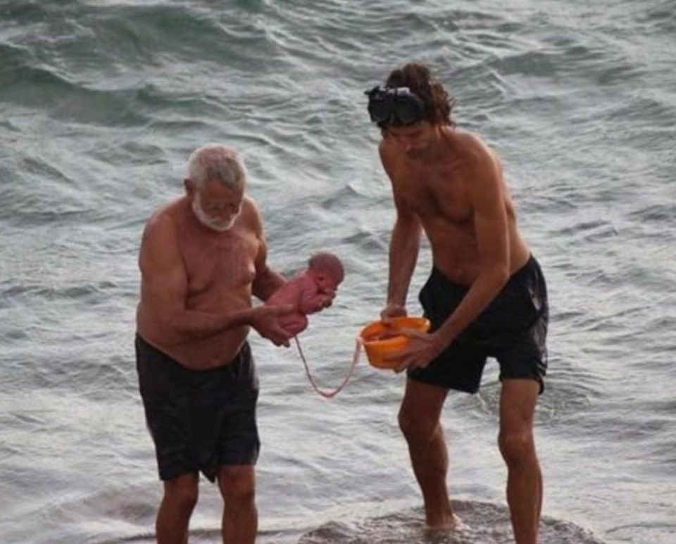 The two men carry the baby out of the water and back to the beach