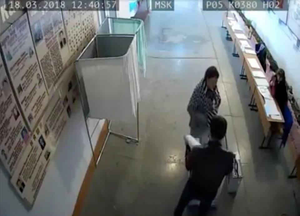 A woman stands guard as a man appears to push slips into a ballot box at an empty polling station