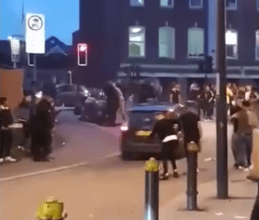  Just in front of the car, people can be seen gathered around one of the victims lying stricken on the floor