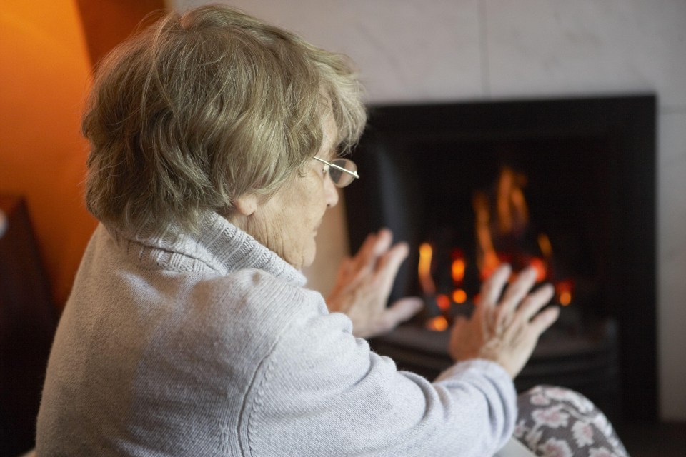 an elderly woman sitting in front of a fireplace warming her hands