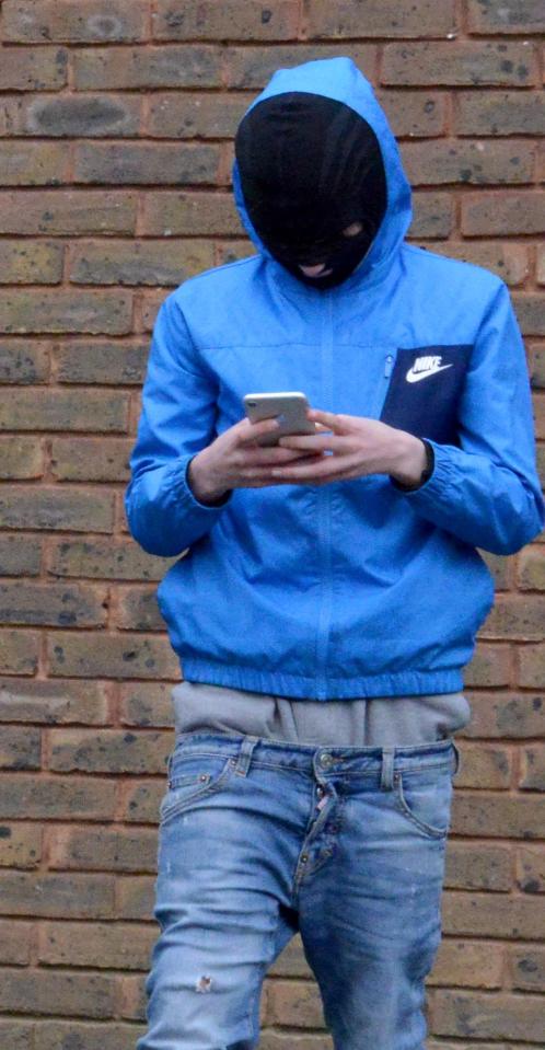  A masked man is pictured using his mobile phone at the scene the morning after the fatal shooting