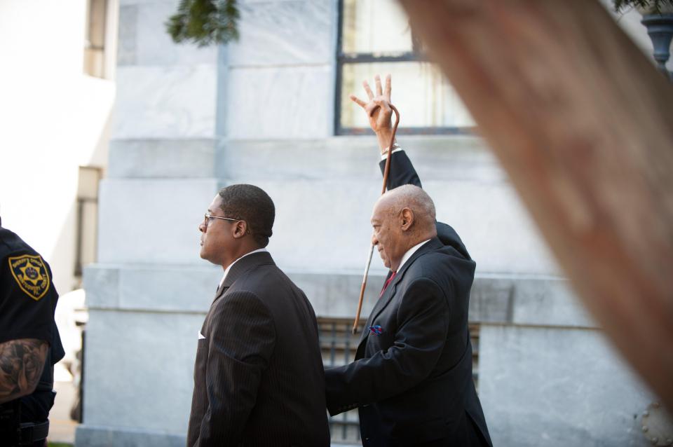  Cosby lifts up his arm with a walking stick in his hand while leaving court earlier today