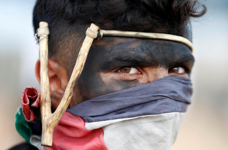  A protester with a slingshot covers his face with a Palestinian flag today