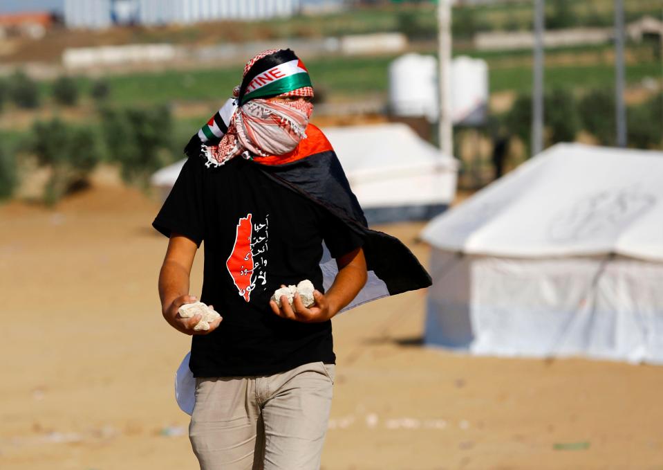  A masked man gathers rocks to hurl as missiles towards Israeli troops