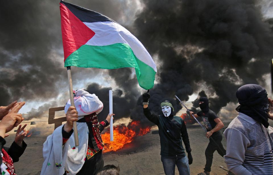  Masked protesters wave a Palestinian flag as tyres burn around them