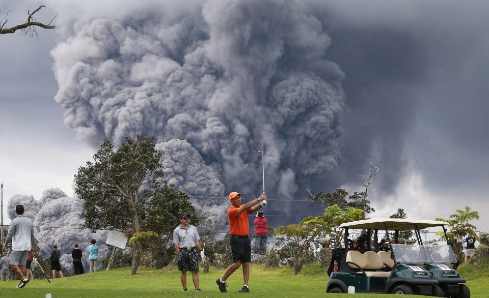  People play golf as an ash plume rises in the distance from the Kilauea volcano on Hawaii's Big Island