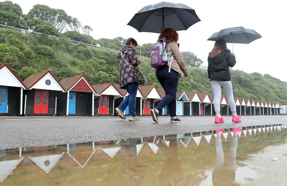  People shelter under umbrellas as they walk past Dorset's Bournemouth beach