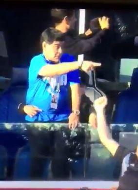 Maradona can be seen handing something off in front of his VIP box before pointing to the crowd and then pointing to his chest