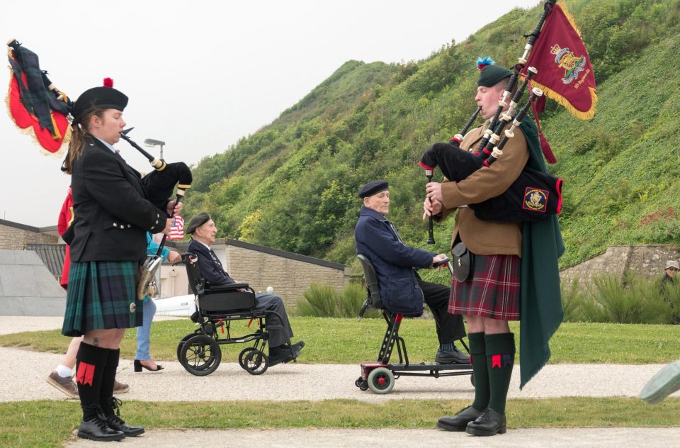  Two Normandy veterans pass military pipers at the wreath laying at the Tactical Air Force Memorial beside Omaha Beach