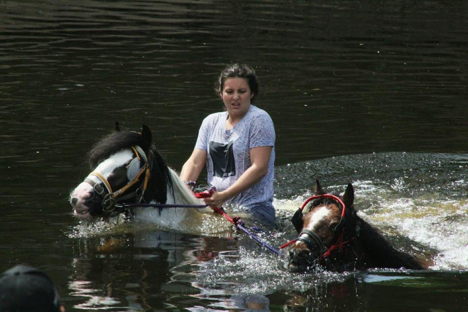  A traveller girl rides one horse while leading another through the water