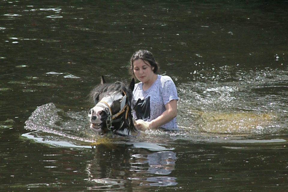  A young traveller girl holds on tight as she rides her horse through the River Eden in Appleby