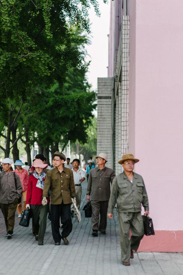  A crowd of men and women walk against North Korea's signature pastel pink background