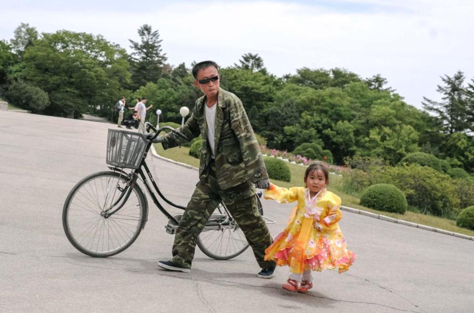  A child dressed in traditional North Korean costume holds hand with a man