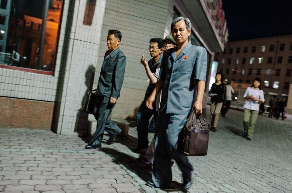  Men carrying briefcases walk through the city in North Korea at night