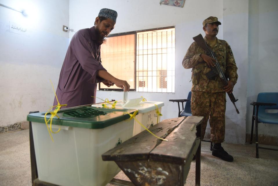 A Pakistani man casts his vote as a soldier stands guard at a polling station during Pakistan's general election in Karachi 