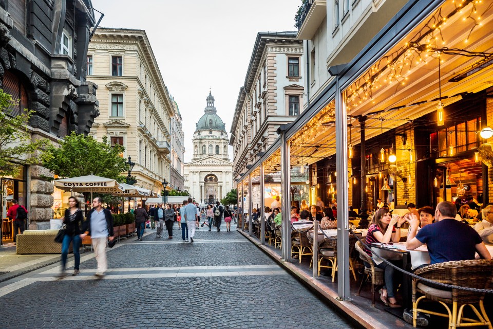 Diners enjoying the restaurants on Zrinyi Utca in Pest with St. Stephen's Basilica in the background.