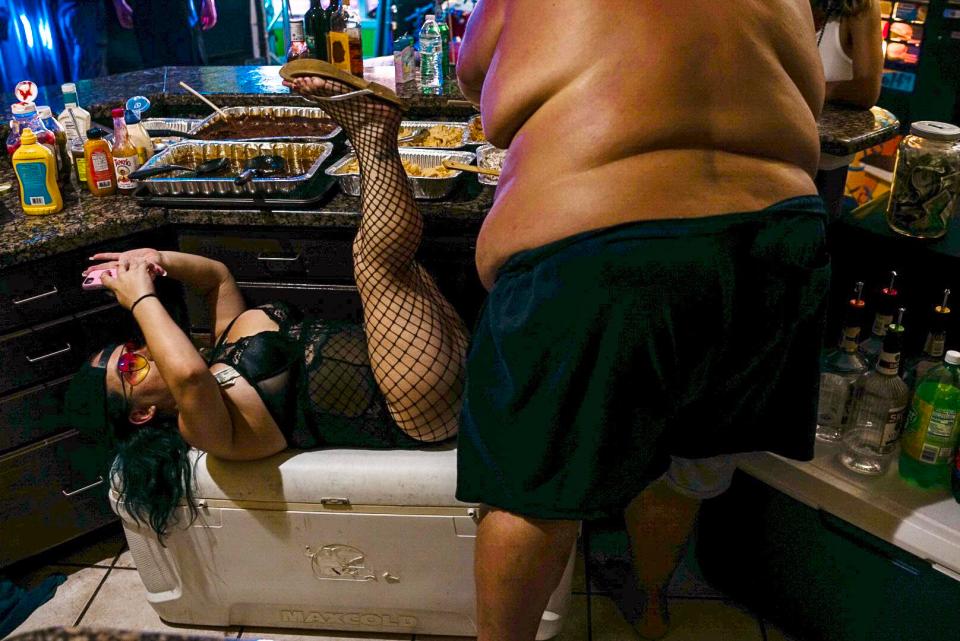  A woman reclines on an ice box to take a selfie while a portly gentlemen grabs a drink from the bar