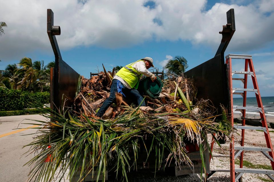  Workers remove debris from a beach in Dorian's path