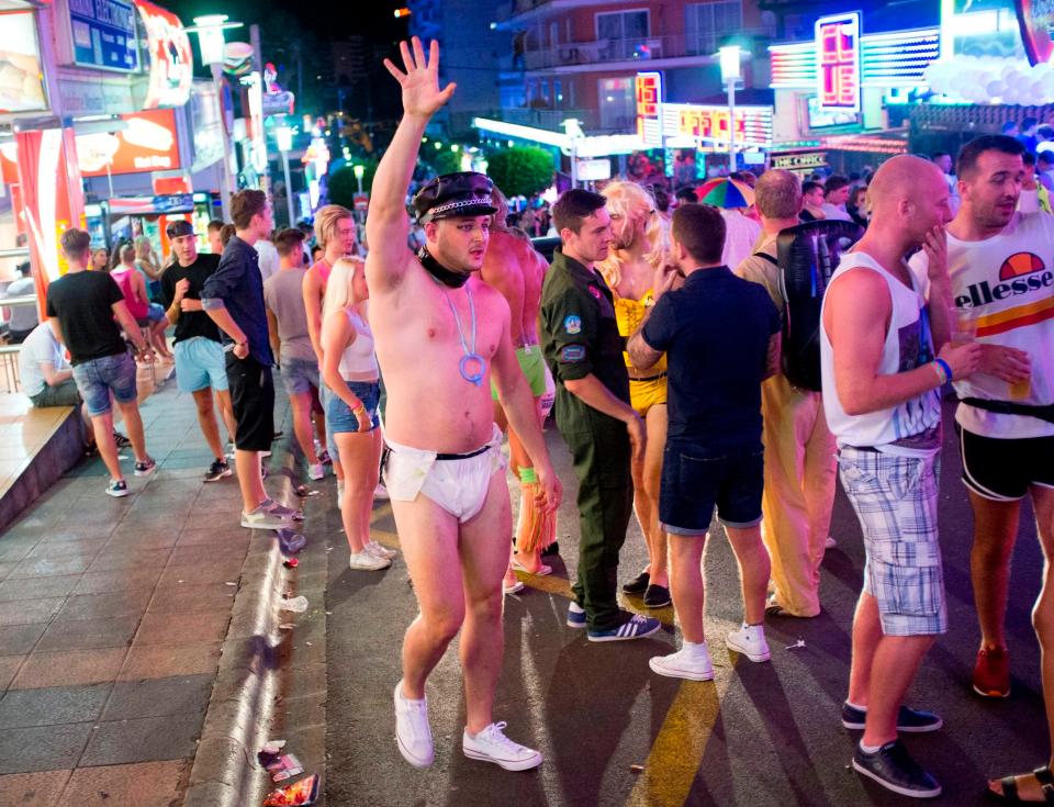  A Brit tourist in fancy dress gestures to a mate on the main clubbing strip during a night of heavy boozing