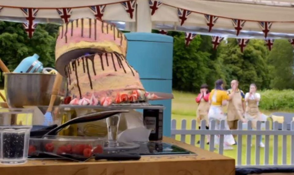  Contestants can be seen in the background with their hands over their mouths as they watch the cake fall