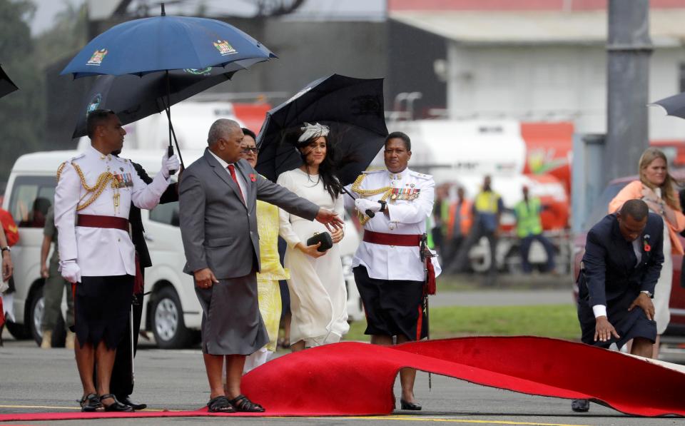  Meghan waits as Fiji PM Frank Bainimarama, left, gestures as a red carpet is laid during the official welcome ceremony