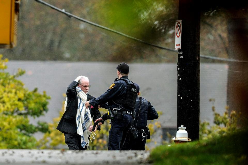  A man holds his head as he is escorted away from the scene by police