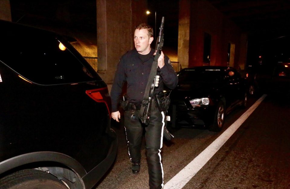  A police officers carries a large firearm at the scene of the shooting