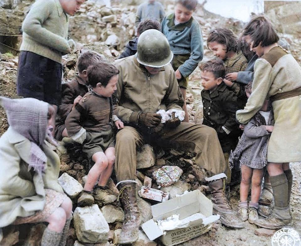  An American soldier sharing wrapped Christmas gifts with local children during the Battle of The Bulge