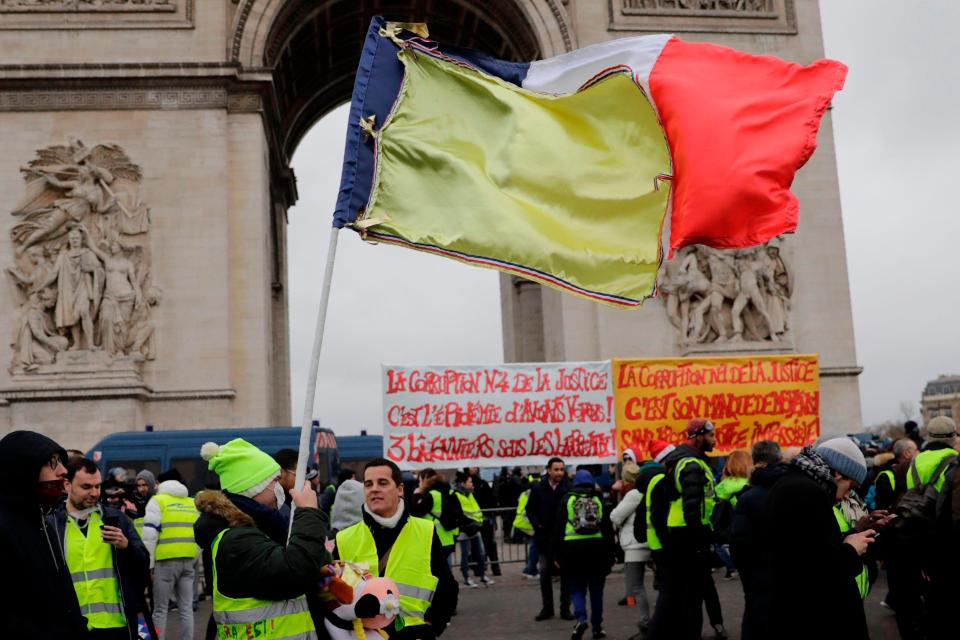  A protester waves a French flag partially covered with a yellow fabric during an anti-government demonstration called by the Yellow Vest movement next to the Arc de Triomphe in Paris