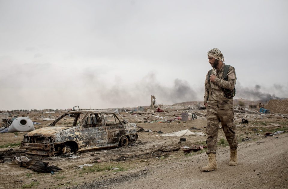  A Syrian Democratic Forces fighter walks past destroyed vehicles in in Baghouz