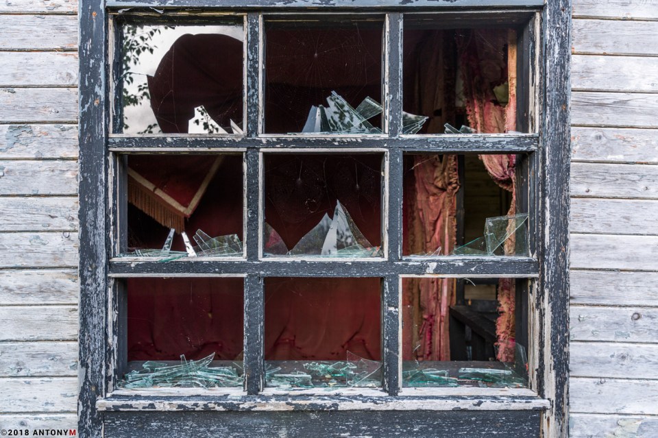 Glass that has been shattered and peeling paint is all that is left of this window