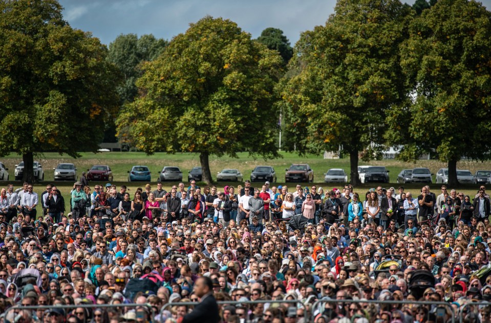 Visitors look on as Muslims attend Friday prayers in a park near Al Noor mosque