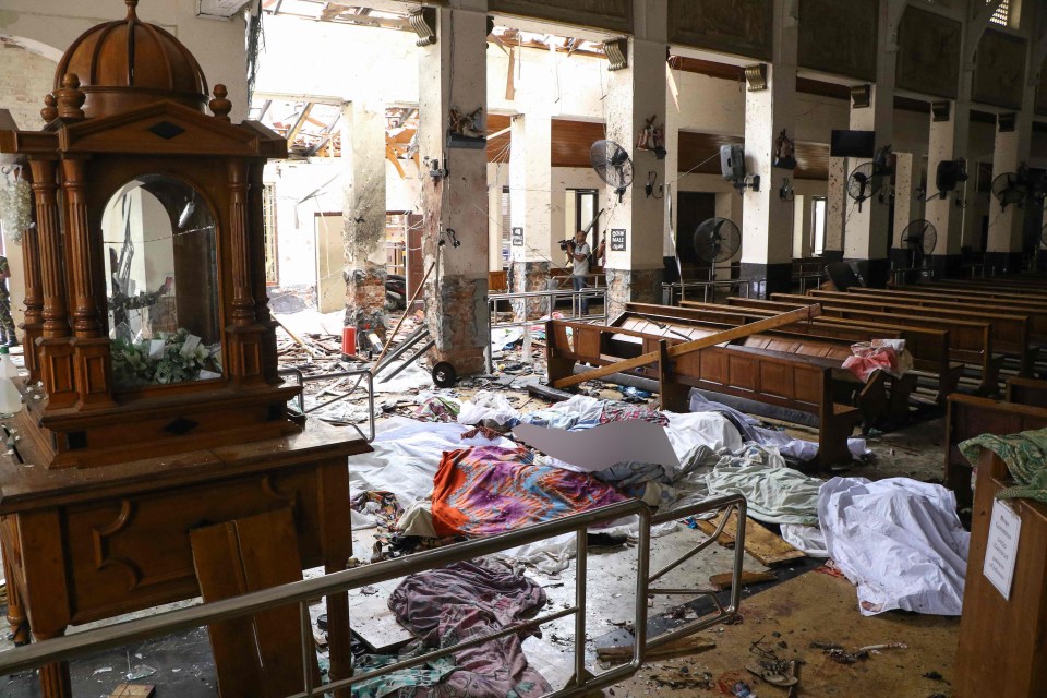  Sri Lankan security personnel walk past dead bodies covered with blankets amid blast debris