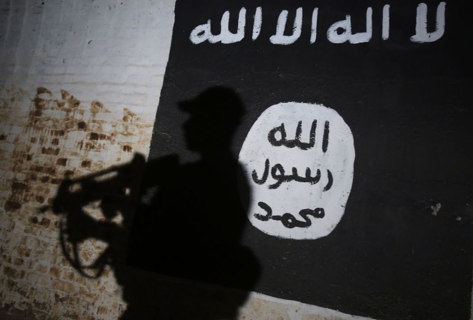  A member of the Iraqi forces walks past a mural bearing the logo of the Islamic State