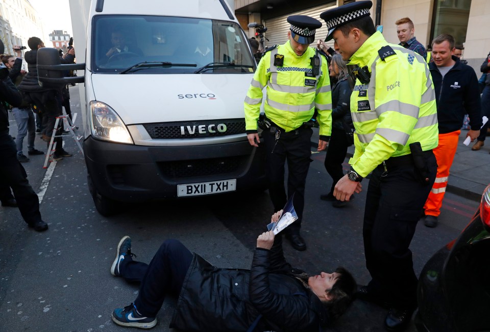  One of Assange's supporters lies on the road in front of the van taking him to court