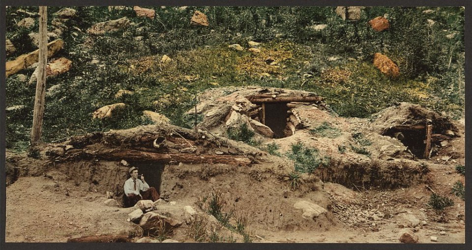 A miner enjoys a smoking break in the entrance to his dug out cabin