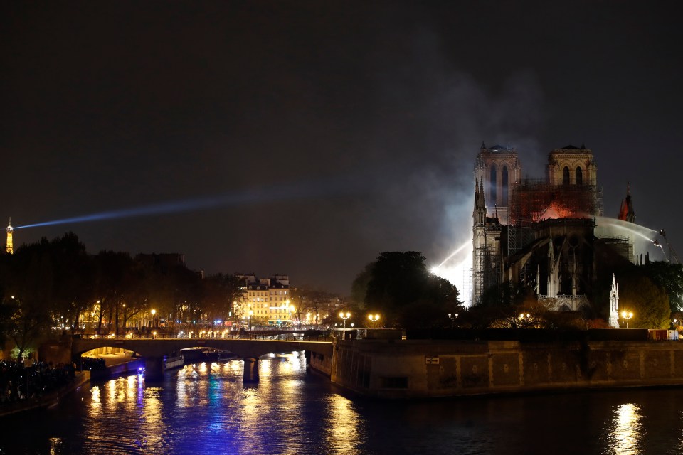  Firefighters douse flames billowing from the roof as Eiffel Tower shines a light onto the famous cathedral