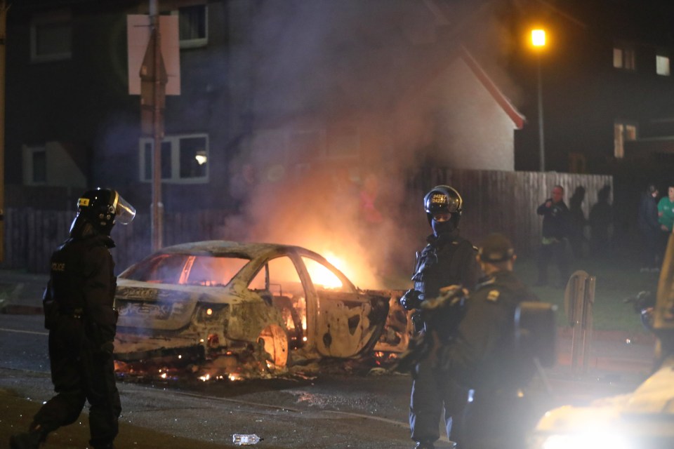 An officer stands by a burning car amid the violence last night