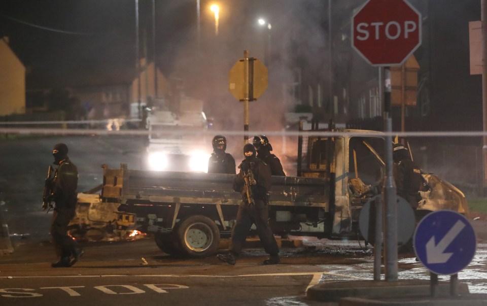 Armed cops by a burnt out vehicle in the Creggan area of the city, where a female journalist was killed last night